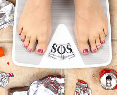 Frau auf Waage, die SOS anzeigt – Übergewicht gehört zu den Sodbrennen-Ursachen