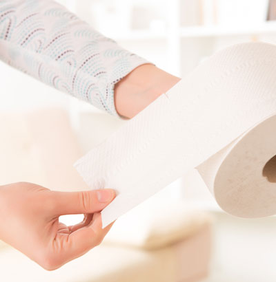 Frau rollt Toilettenpapier ab – Colitis ulcerosa verursacht Symptome wie Durchfall